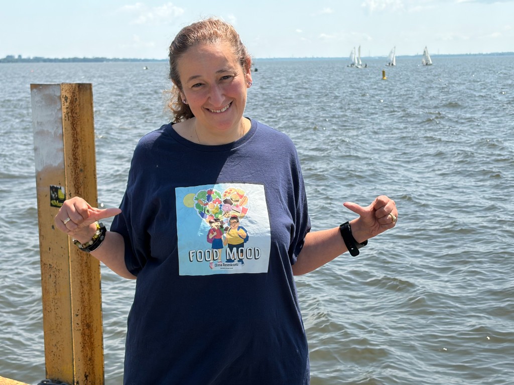 Elissa Rosenkrantz, author of Food Mood, smiling outdoors in a navy t-shirt featuring the Food Mood book cover.